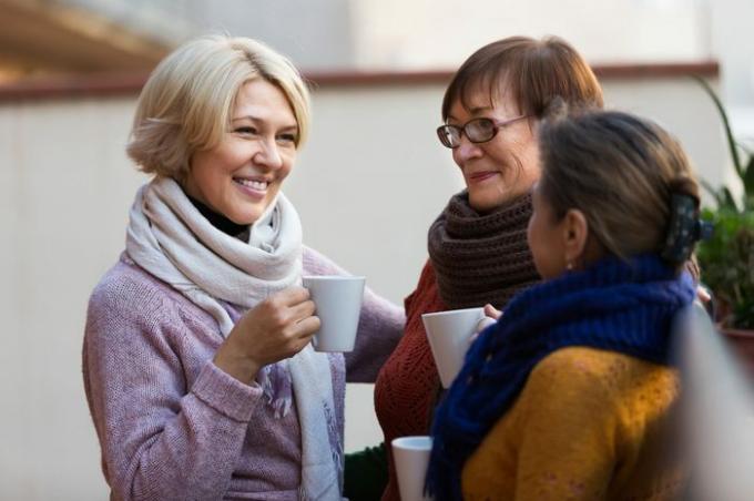 Grupo de sonrientes mujeres maduras bebiendo té en el balcón