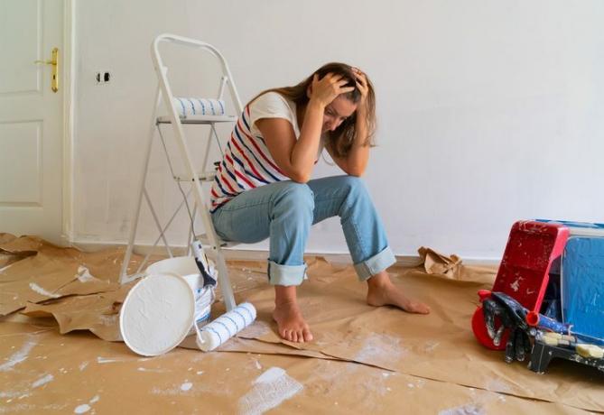 La mujer estresada se sienta en la renovación del dormitorio con un desorden de pintura a su alrededor en el piso
