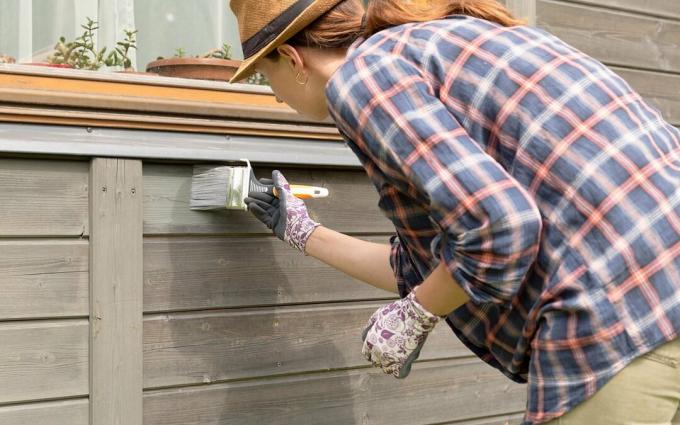 Travailleuse peignant le mur extérieur de maison en bois avec le pinceau et la couleur protectrice en bois