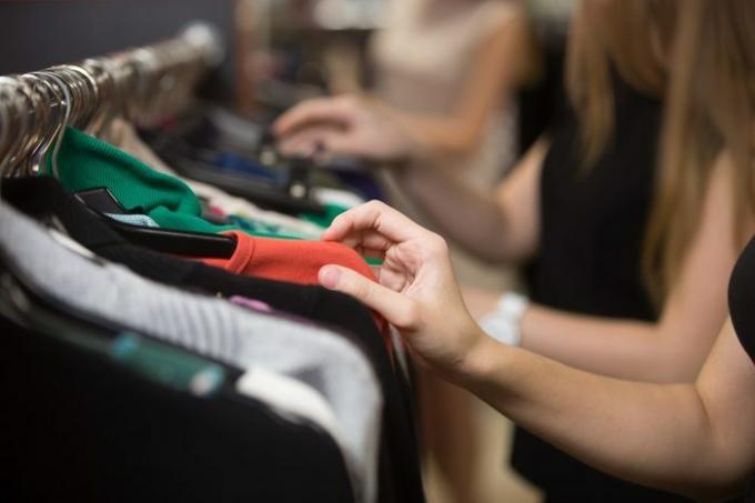 Молодые красивые женщины делают покупки в торговом центре моды, выбирают новую одежду, просматривают вешалки с различными повседневными красочными предметами одежды на вешалках, крупным планом рук
