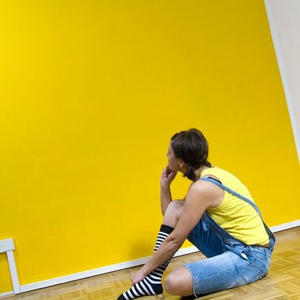 Donna seduta sul pavimento, guardando il muro giallo