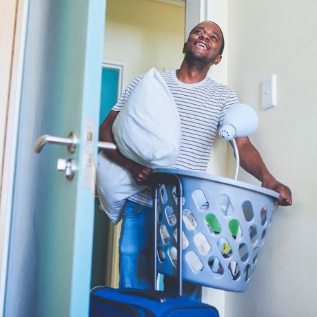 Estudiante con una canasta de lavandería con suministros para el dormitorio.