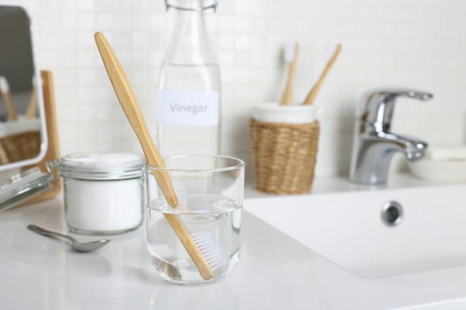 تنظيف فرشاة الأسنان بالخل الأبيض والماء ومحلول صودا الخبز على حوض الحمام عن قرب.