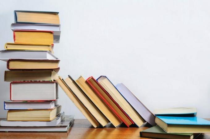 Įvairių knygų krūva ant stalo baltos sienos fone