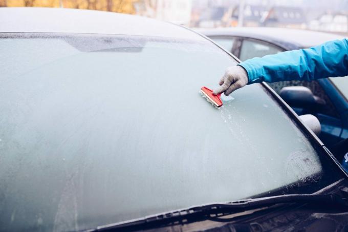 Kvinne som fjerner is fra bilruten med glassskrape. Frostig morgen