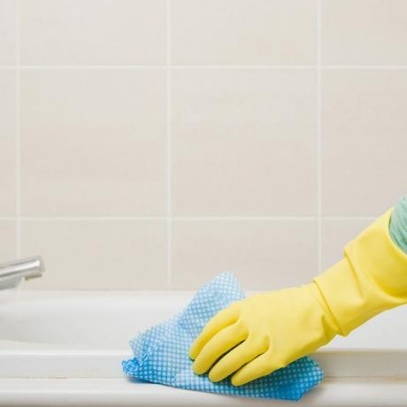 Cerca de guante de goma limpieza de manos y baldosas del baño y lechada