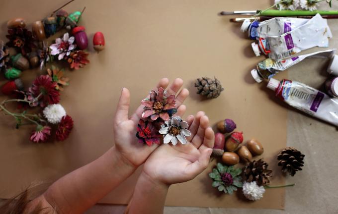 Söpö pieni 5-6-vuotias tyttö, joka värittää luonnollista kartionkuusta luodakseen kukan, harjat, maalit, luonnolliset syksyn materiaalit pöydälle, luomaan hauskaa ja helppoa lasten kanssa, DIY päiväkotiin
