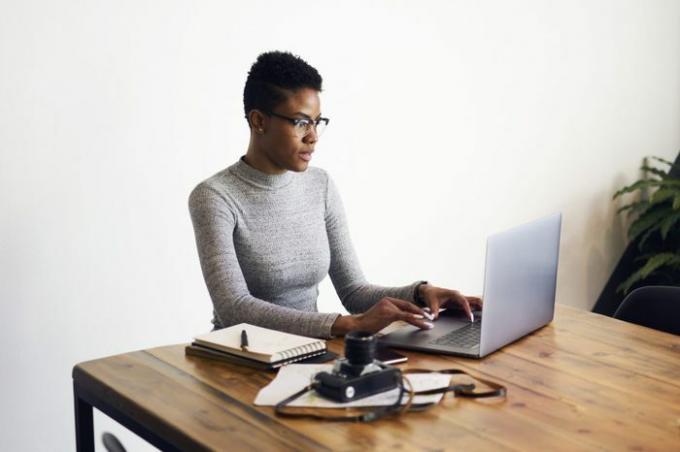 Privlačna afroameriška poslovna ženska, ki uporablja prenosni računalnik za spletno delo in opravlja delo na daljavo v coworking prostoru, profesionalni fotograf ureja slike prek aplikacije na prenosnem računalniku