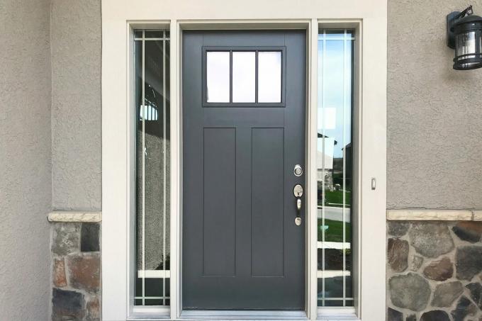 Циментово сива предна врата с бяла облицовка, прозорци от двете страни на вратата, гипсова облицовка и скален камък, залепен в предната част на дома