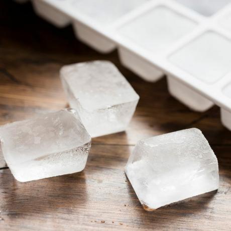 Miska na kocky ľadu naplnená kockami ľadu a tromi stratenými kockami ľadu proti tmavému drevu.
