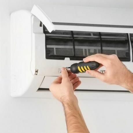 Mannelijke technicus die airconditioner binnenshuis repareert