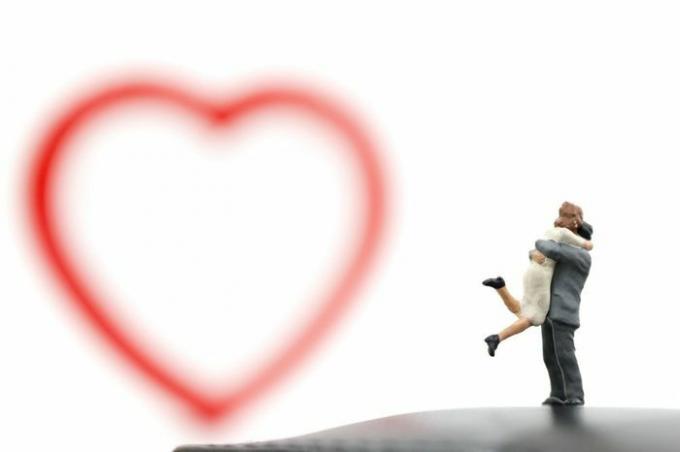 Casal em miniatura se abraçando e coração vermelho em fundo branco, conceito de dia dos namorados