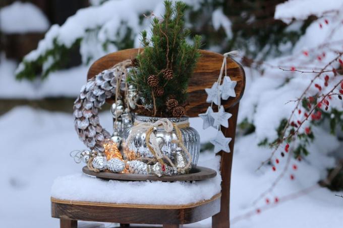 Winterkomposition mit Weihnachtskranz, Glasdekoration, Girlande, Tannenbaum, Holzstern auf Vintage-Holzkinderstuhl auf Schnee, natürlicher Hintergrund, Außen- und Raum, Szene im Schneegarten