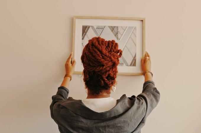 Aufnahme einer nicht wiederzuerkennenden Frau, die zu Hause ein Gemälde aufhängt