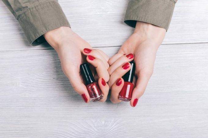 Пляшки з червоним лаком для нігтів у жіночих руках вид зверху