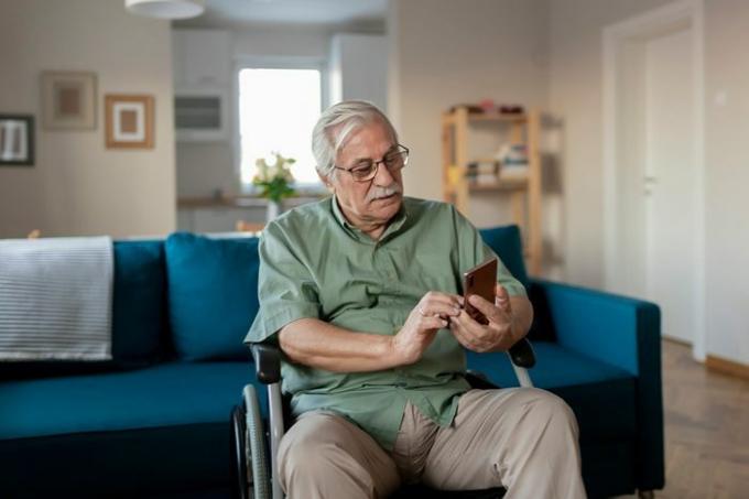 Hombre mayor discapacitado sentado en una silla de ruedas y con un teléfono inteligente