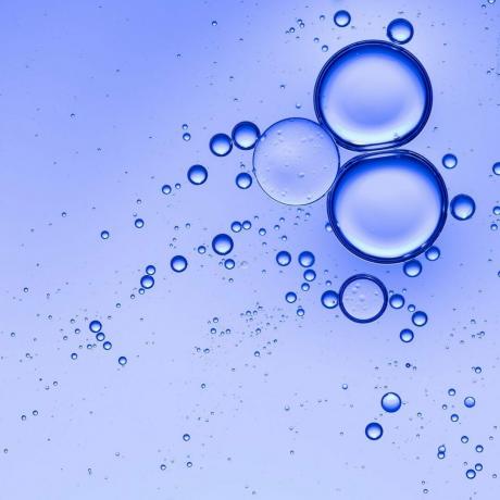 파란색 배경을 가진 물 위에 떠 있는 기름 방울과 거품