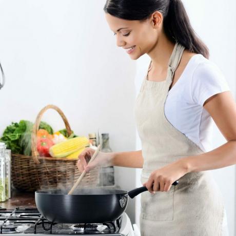 台所のストーブのそばに立って、鍋で食事から素敵な香りを調理し、匂いを嗅ぐ女性