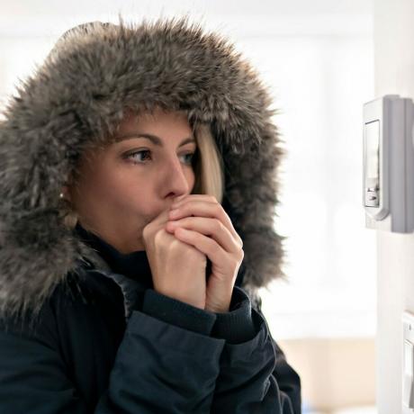 Wanita mengenakan jaket musim dingin di dalam ruangan, memeriksa termostat