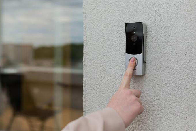 moters ranka naudoja durų skambutį ant namo sienos su stebėjimo kamera