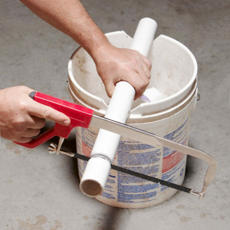 Verwenden Sie einen Eimer, um das PVC-Rohr abzustützen, während Sie das Rohr mit einer Metallsäge schneiden