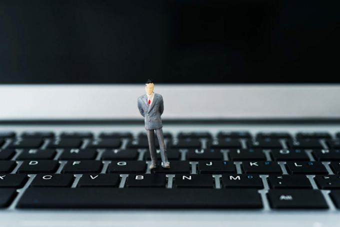 Miniaturní podnikatel stojící na klávesnici notebooku.