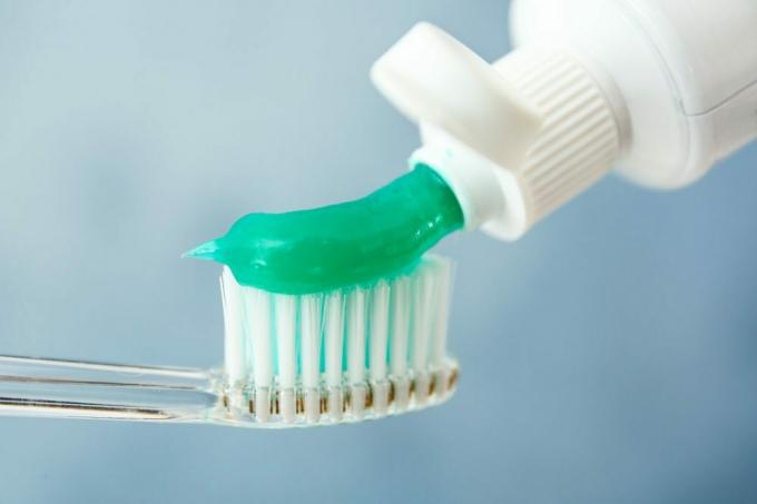 Exprimir la pasta de dientes en el cepillo contra el fondo de color, primer plano