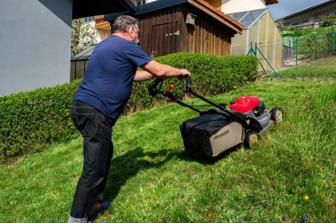 Een man maait het gras in zijn tuin met een Honda HRX76 grasmaaier.