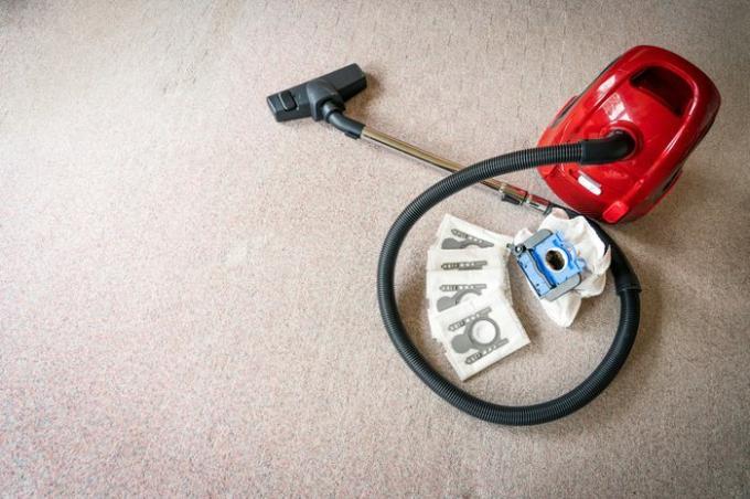 Un limpiador de vacío rojo con bolsas de filtro de vacío nuevas y viejas sobre un piso de alfombra blanca con espacio a la izquierda para el texto. Concepto de limpieza y mantenimiento.