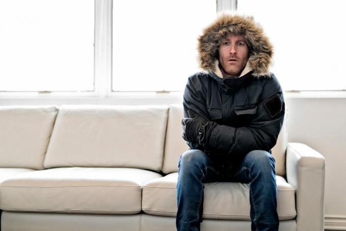 vyras su žieminiu paltu sėdi ant sofos