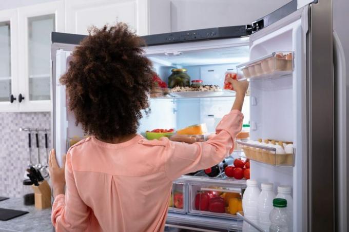 냉장고에서 음식을 먹는 젊은 여자의 후면보기