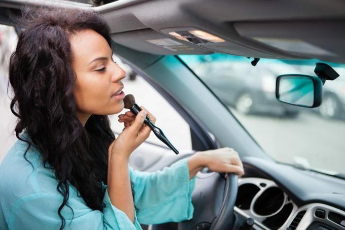 Atractiva mujer joven retocando su maquillaje en un coche mirando en el espejo retrovisor