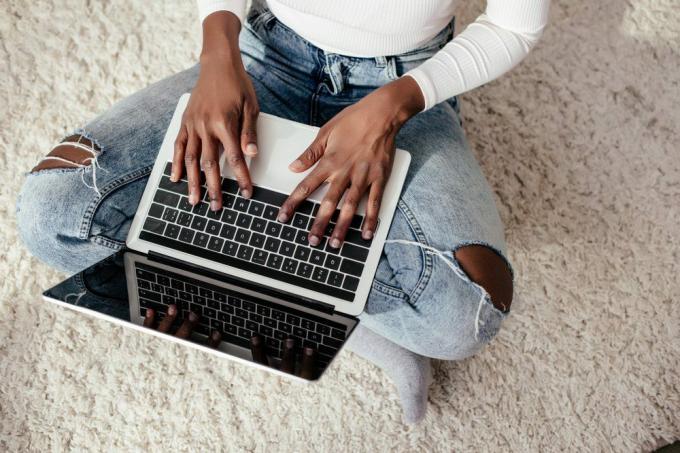 изрязано изображение на афроамериканка, използваща лаптоп на пода у дома