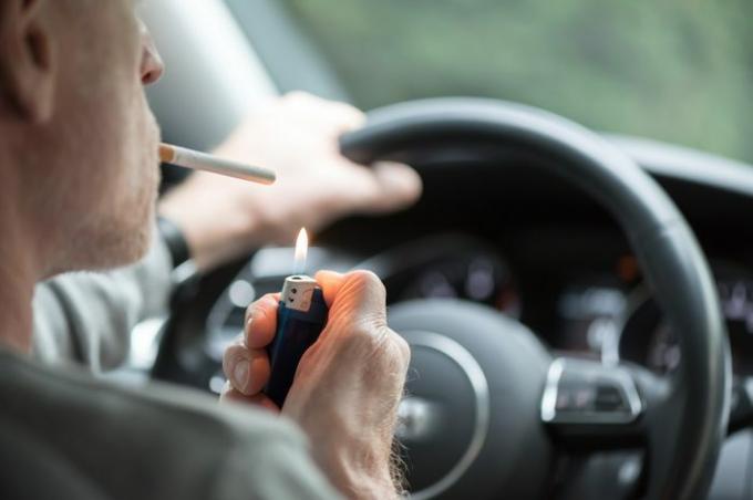 Muž, ktorý šoféruje, zapaľuje si cigaretu