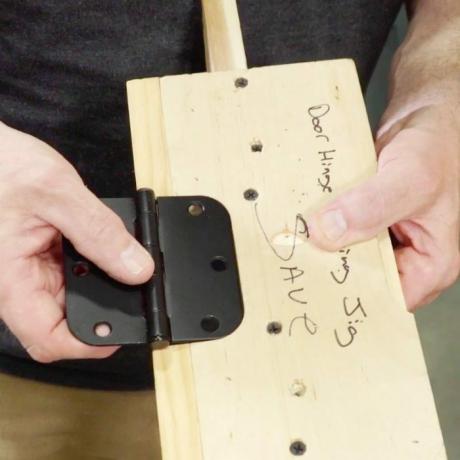 manos sosteniendo una bisagra en un trozo de madera haciendo una plantilla de bisagra de puerta