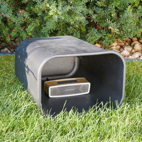 uma lata de lixo na horizontal em um gramado com um alto-falante bluetooth dentro
