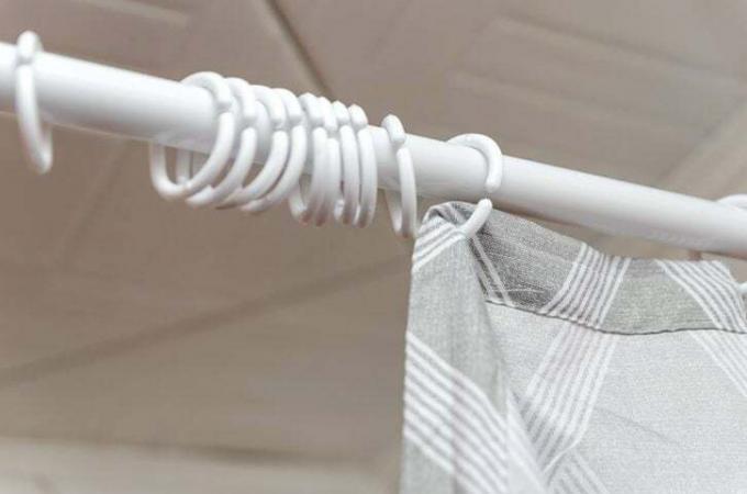 Close-up van een onvolledige ophanging van een grijs gordijn in de badkamer met douche