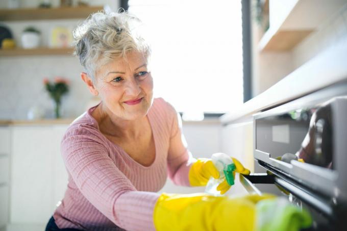 집에서 실내에 있는 노인 여성의 전면 전망, 주방 청소.