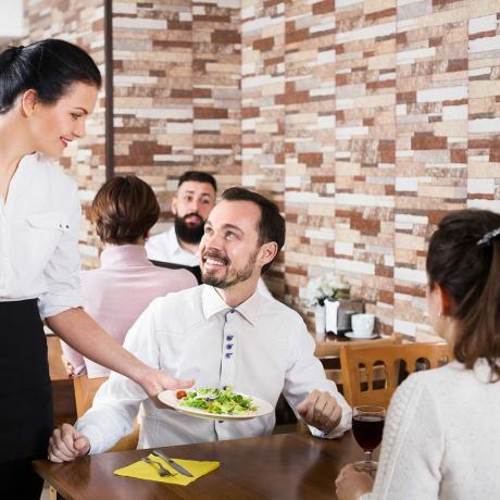 Positieve serveerster die tafelbestelling neemt en lacht in de taverne?