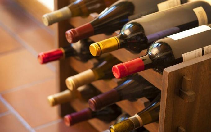 Bottiglie di vino rosso e bianco impilate su scaffalature di legno riprese con profondità di campo limitata