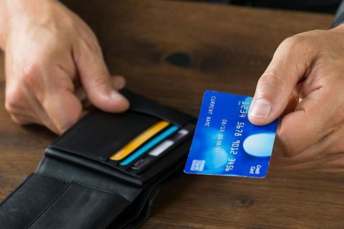 Immagine ritagliata dell'uomo d'affari che dà la carta di credito dal portafoglio alla scrivania