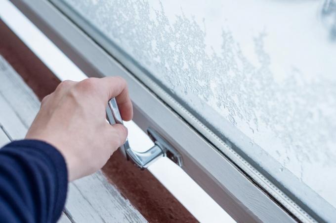 Persons håndsveiv som åpner vindu om vinteren med is mot glassvinduene og snødekt bakgrunn