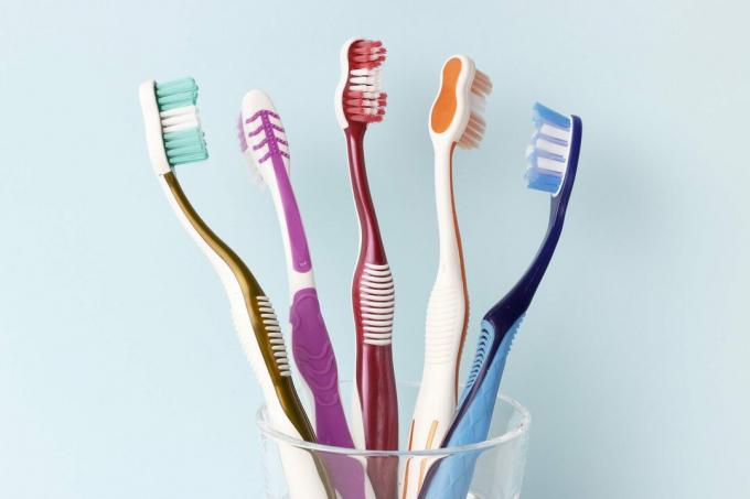 Cam bardak ön görünümünde çok renkli diş fırçaları, mavi arka plan