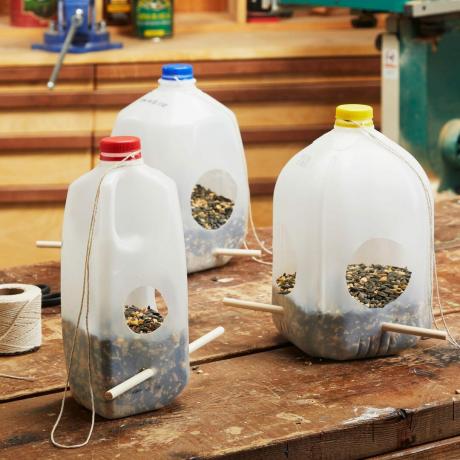 tres comederos para pájaros con jarra de leche de diferentes tamaños llenos de semillas para pájaros sentados en un banco de trabajo