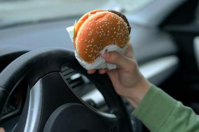 Közelkép a vezető kezét a volánnál, miközben ételt eszik a forgalomban