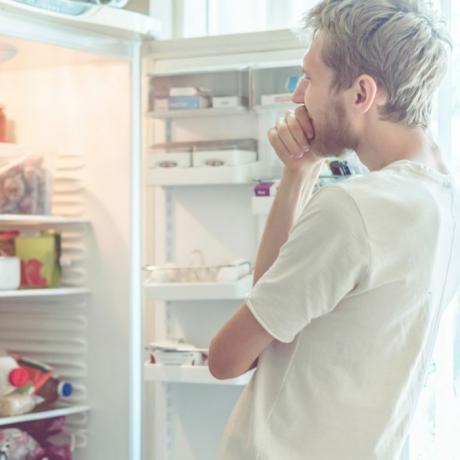 pemuda mencari makanan di lemari es di rumah
