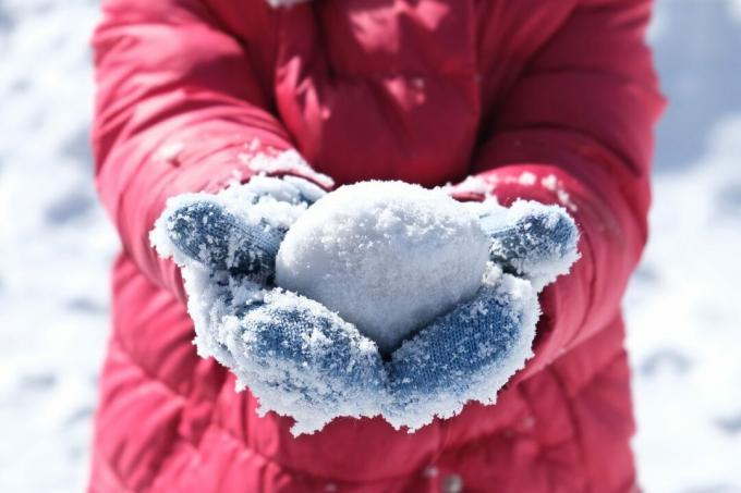 Bulgăre de zăpadă în mănuși înghețate pe mâinile unui copil