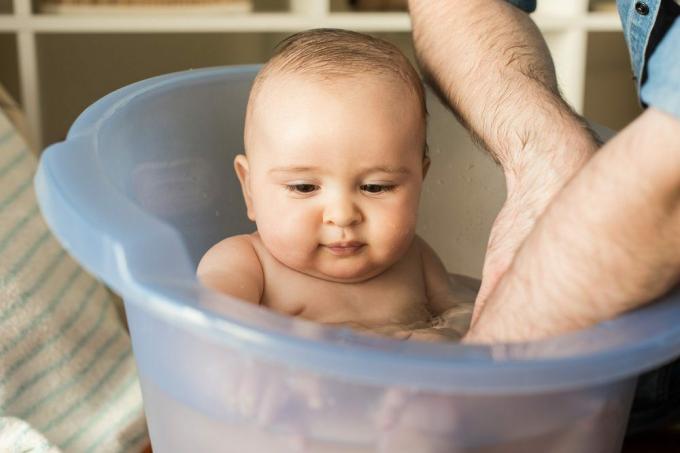 Padre moderno che bagna il suo piccolo bambino con una vasca per la pancia