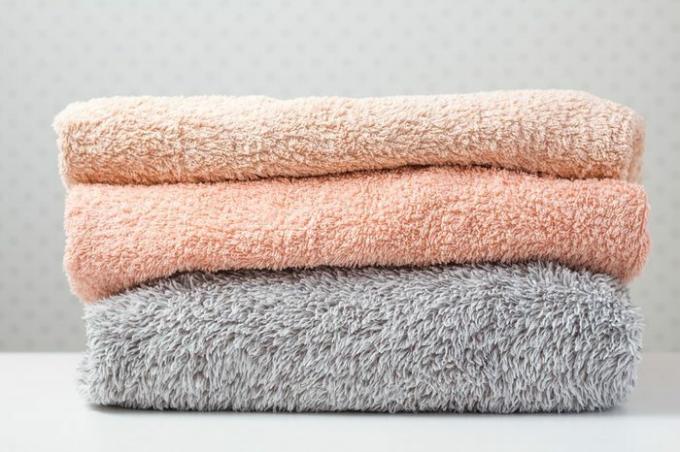 Asciugamani da bagno di diversi colori in cesto di vimini su sfondo chiaro