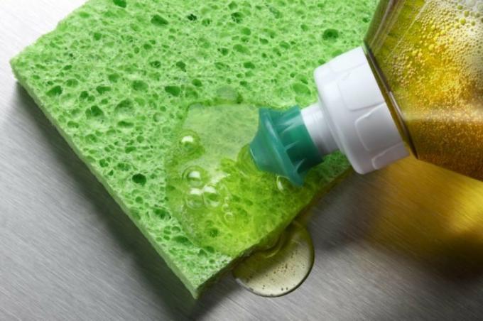 macroschot van afwasmiddel dat op groene spons in aluminiumgootsteen wordt geperst